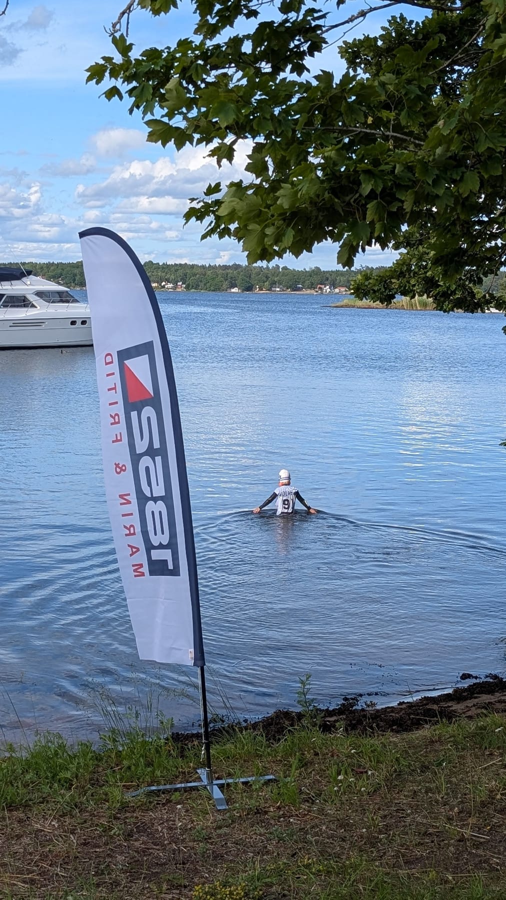 1852 Marin & Fritid sponsorflagga vid Dragsös strand, swimrunåkare på väg ut i vattnet